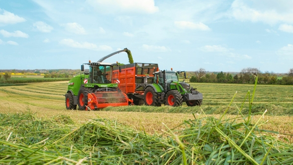 Ein Fendt Katana beim Häckseln auf einer Wiese, rechts daneben ein Fendt Traktor mit Ladewagen.