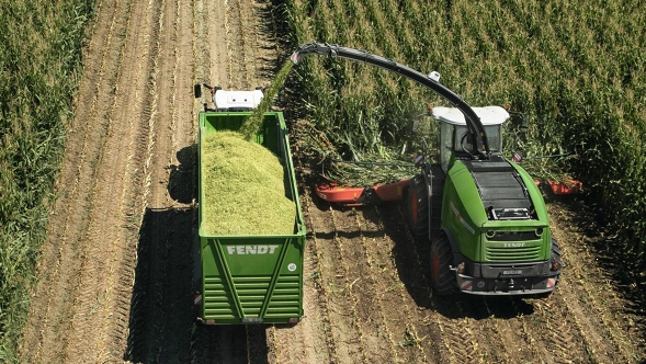 Ein Fendt Katana Feldhäcksler und ein Fendt Traktor mit Fendt Tigo Ladewagen auf einem Maisfeld.