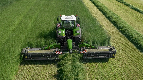 Ein Fendt Traktor mit Fendt Slicer Mähwerk auf einer grünen Wiese aus der Vogelperspektive.