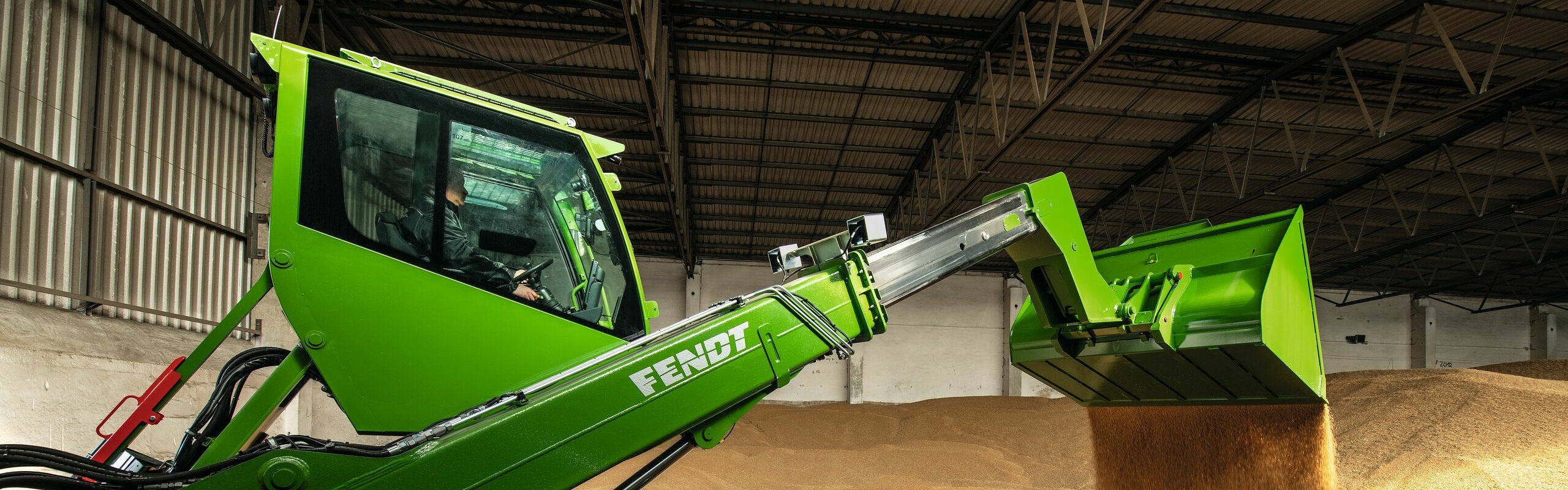 Ein Landwirt steht mit einem Fendt Cargo T955 in einer Lagerhalle und schüttet mit der Schaufel Getreide aus.