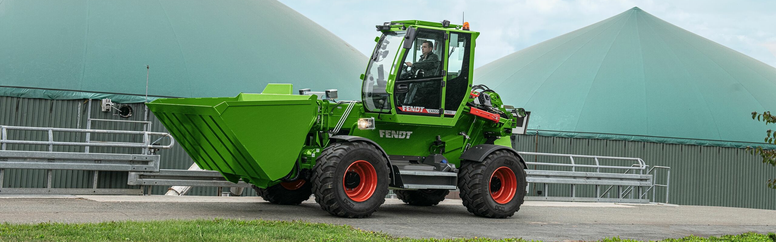 Ein Landwirt fährt mit einem Fendt Cargo T955 auf einem Weg vor einer Biogasanlage.