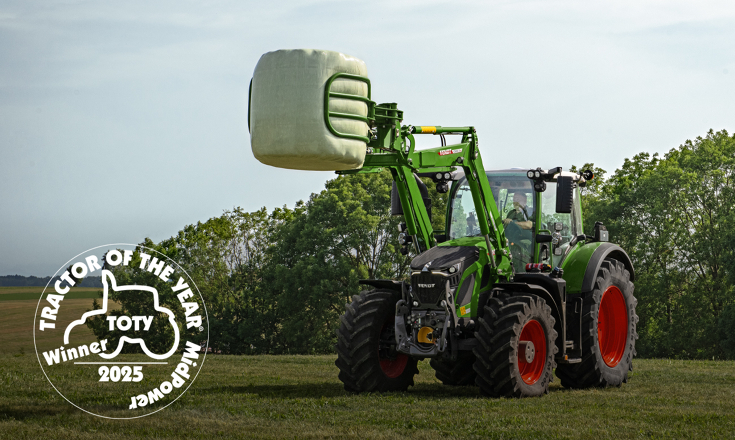 Fendt 620 Vario mit angehobenem Fendt Frontlader auf einer Wieser mit einem Rundballen in der Ballenzange - vorne links ist das Logo desractors of the Year in der Kategorie MidPower in weiß platziert