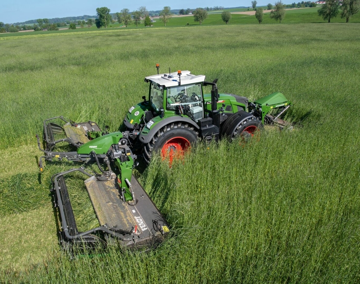 Ein Fendt Traktor fährt mit der Mähwerkskombination Fendt Slicer 960 KCB Pro durch hoch stehendes Gras im Grünland und mäht