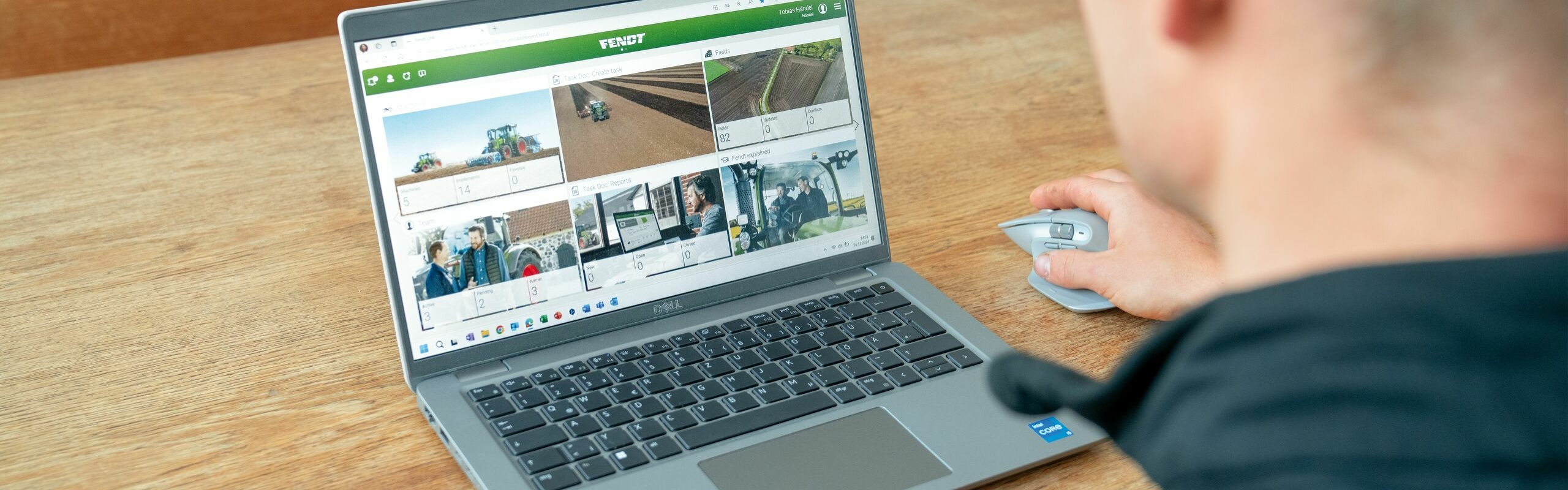 Ein Mann bedient mit einer Maus ein geöffnetes Notebook, das auf einem hellbraunen Holztisch steht. Auf dem Bildschirm ist die Plattform FendtOne Offboard geöffnet, die verschiedene Daten anzeigt.
