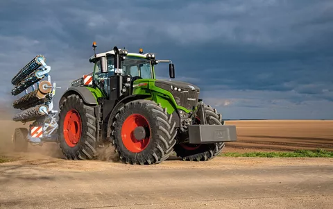 Fendt 1000 Vario kører med redskab på en vej ved siden af en mark