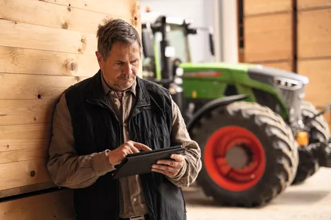 Mand kigger på IPad med en Fendt-traktor i baggrunden