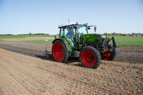 En Fendt e107 Vario trækker sort afdækningsfolie over jordbærbede på en mark, føreren er en ældre landmand med hvidt hår.