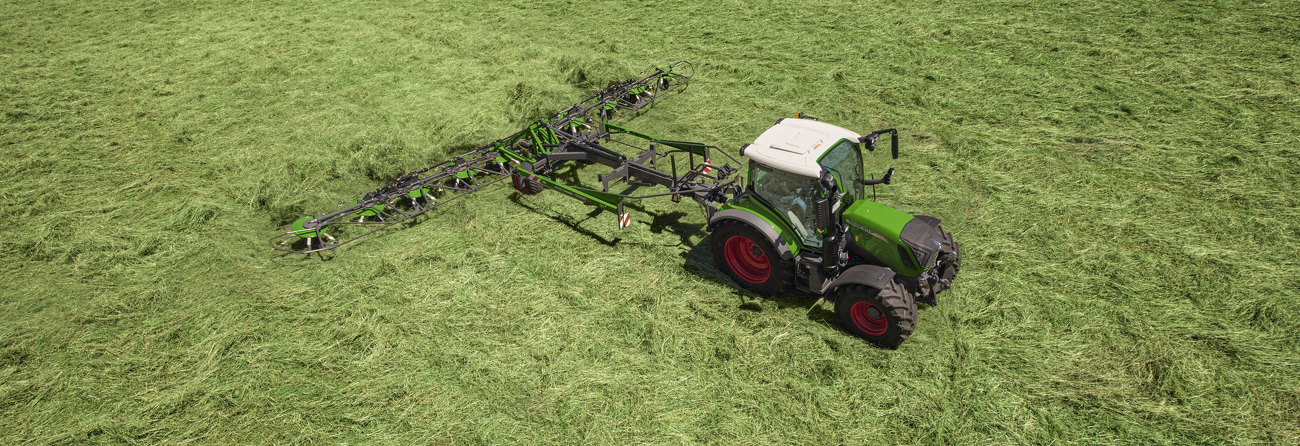 Et grønt Fendt Lotus redskab på en grøn Fendt traktor med røde fælge under arbejde med græshøst i en grøn eng.