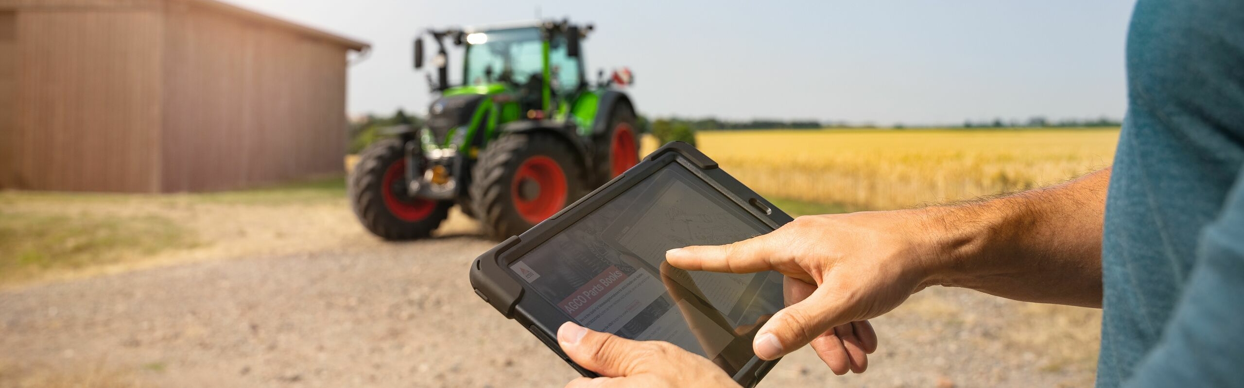 En landmand bruger en Fendt Service App på sin tablet, i baggrunden ses hans grønne Fendt 700 Vario