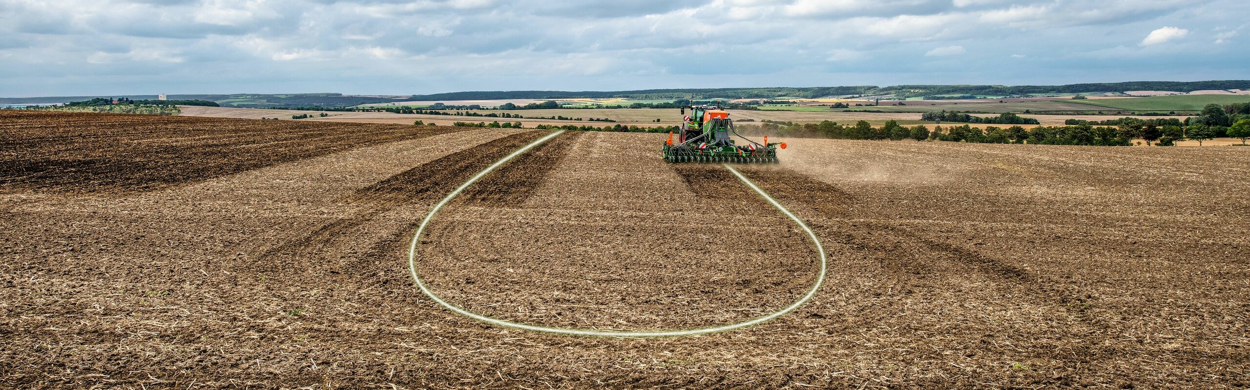 Landskabsbillede over en åben mark og en Fendt traktor under jordbearbejdning med FendtONE autostyring