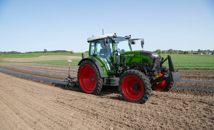 En Fendt e107 Vario trækker sort afdækningsfolie over jordbærbede på en mark, føreren er en ældre landmand med hvidt hår.