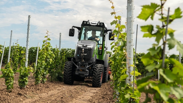 En Fendt e100 V Vario kører i vinmarker med en såmaskine.