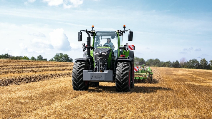 Fendt 700 Vario Gen 7 på arbejde på en mark. I baggrunden er der træer og en blå himmel med hvide skyer.