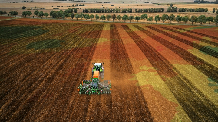 Vaade linnulennult põllule, millel sõidab roheline Fendti traktor koos võrku ühendatud rippmasinaga ning kasutades paralleelsõidusüsteemi.