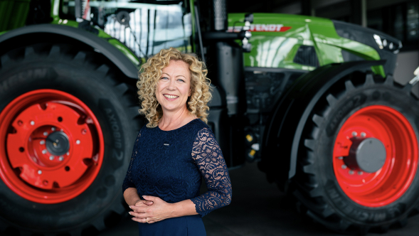 Ingrid Bußjäger-Martin posa con un vestido azul oscuro delante de un tractor Fendt