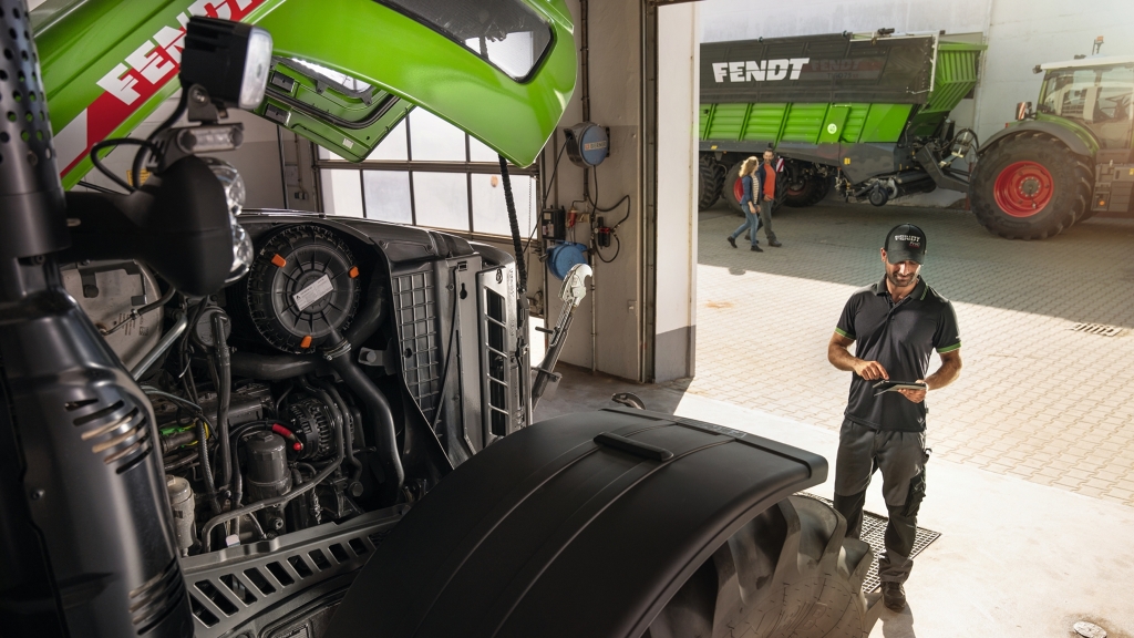 Un trabajador del servicio técnico en el taller del concesionario Fendt con clientes al fondo