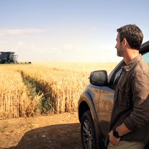 Un agricultor está en un campo de cereal y mira su segadora-trilladora IDEAL, que financió con AGCO Finance