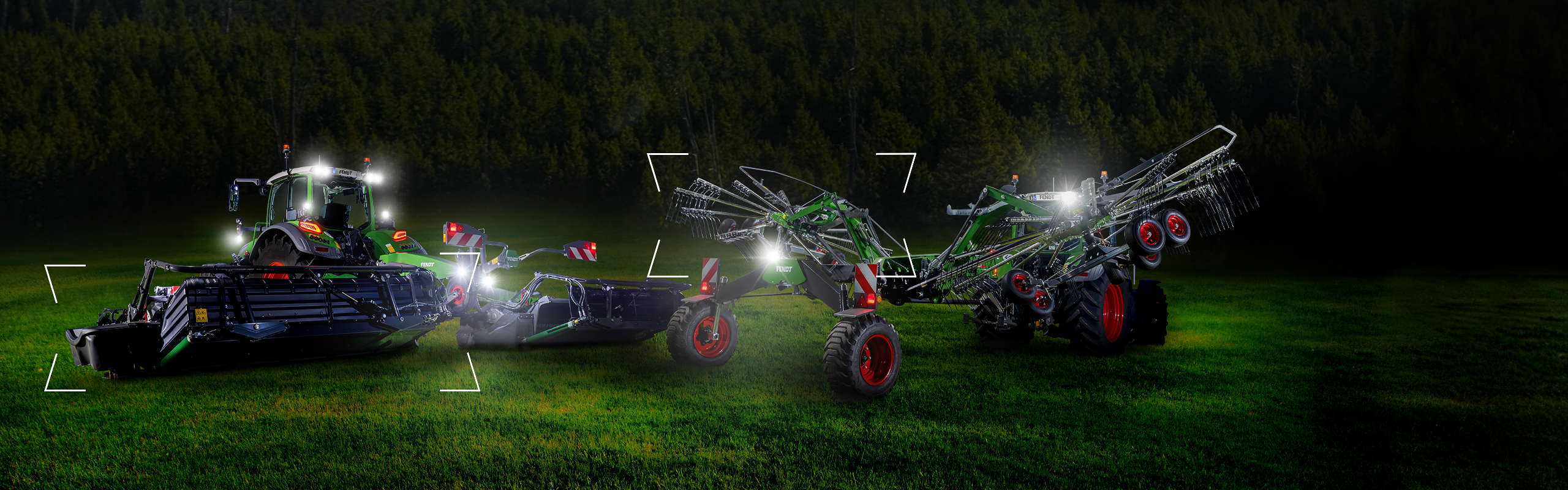 Dos tractores con una segadora Fendt Slicer y un rastrillo Fendt Former se encuentran en el prado al anochecer y están iluminados.