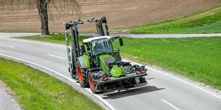 Un agricultor circula por la carretera con una segadora trasera Fendt Slicer plegada y una segadora frontal Fendt Slicer.