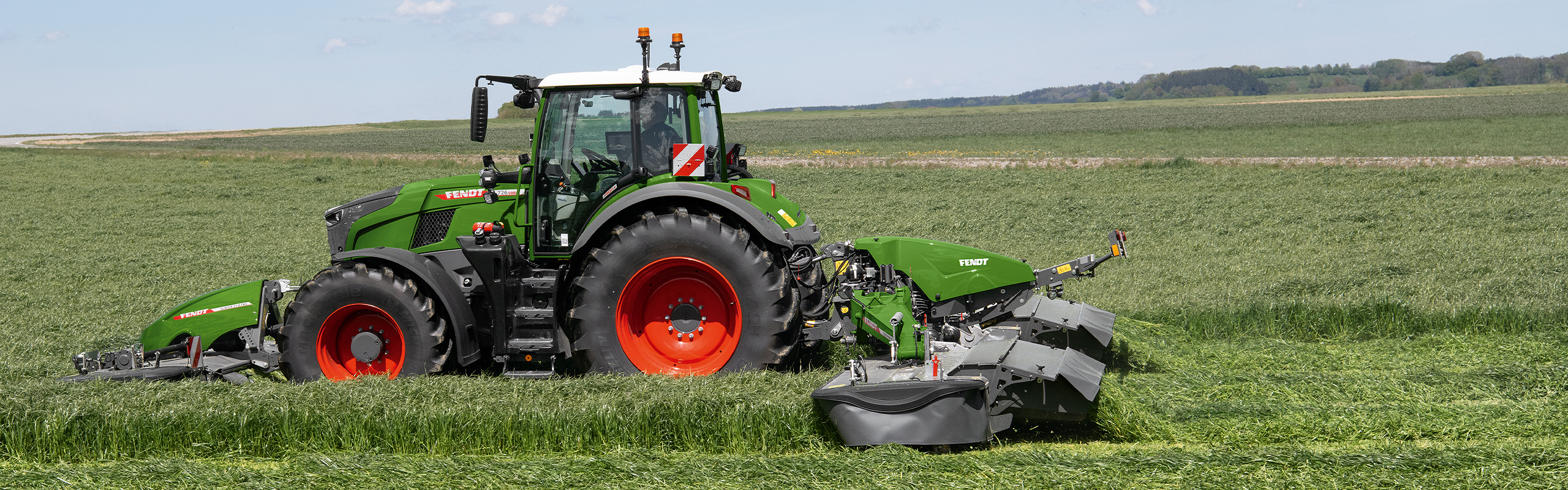 Combinación de acondicionadora y segadora Fendt Slicer en uso en el campo. Al fondo se ven un maizal y árboles.