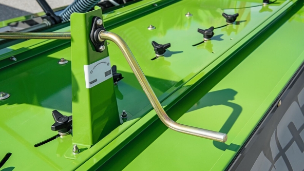 Un tractor Fendt verde con una Fendt Slicer remolcada con chasis de transporte en una carretera comarcal. En el fondo se ve el cielo azul con nubes blancas y un bosque.