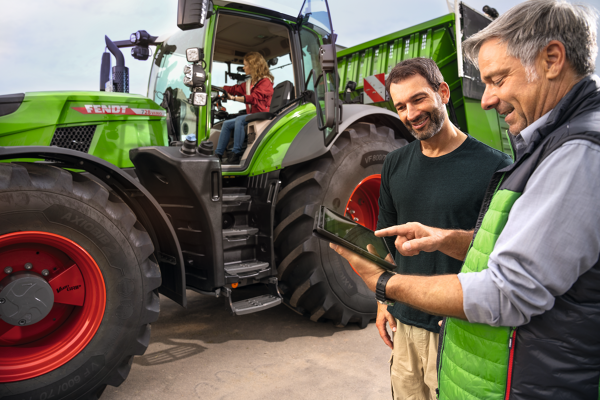 Una agricultora está sentada en un Fendt 700 Vario Gen7 mientras el agricultor está delante del tractor recibiendo asesoramiento de un distribuidor Fendt que tiene una tableta en la mano.