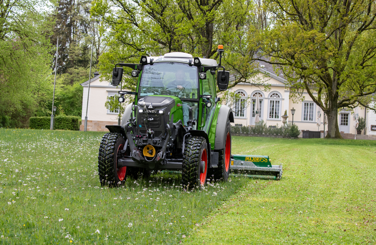 Un Fendt e107 Vario segando un prado en un parque frente a un edificio histórico