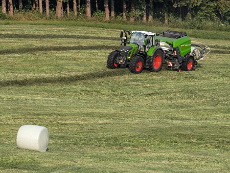 Maanviljelijä ajaa Fendt-traktorilla niityn poikki ja puristaa pyöröpaaleja Fendt Rotanalla.