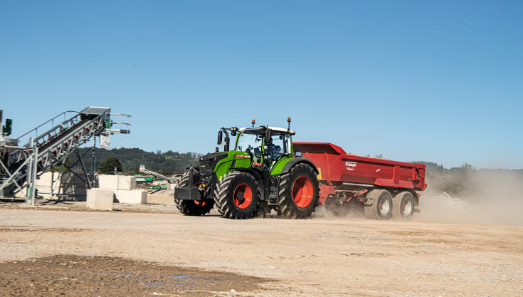 A Fendt 700 Vario Gen7 is driving on a construction site with a red Krampe tipper, raising clouds of dust.