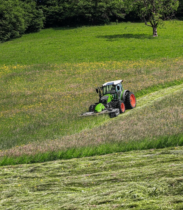 Fendt 200 Vario avec Fendt Slicer dans un terrain vert escarpé lors du fauchage du pâturage.