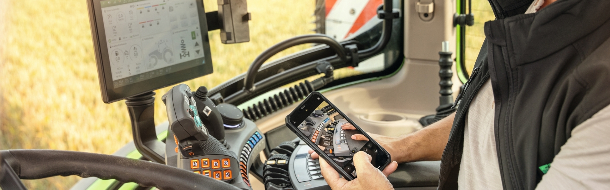 Un agriculteur est assis dans une cabine Fendt, un téléphone portable à la main, et regarde une vidéo explicative de Fendt.