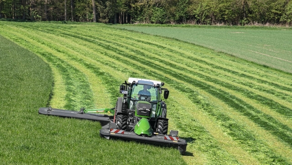 Un Fendt 200 Vario en train de faucher avec un attelage avant et arrière dans les prairies