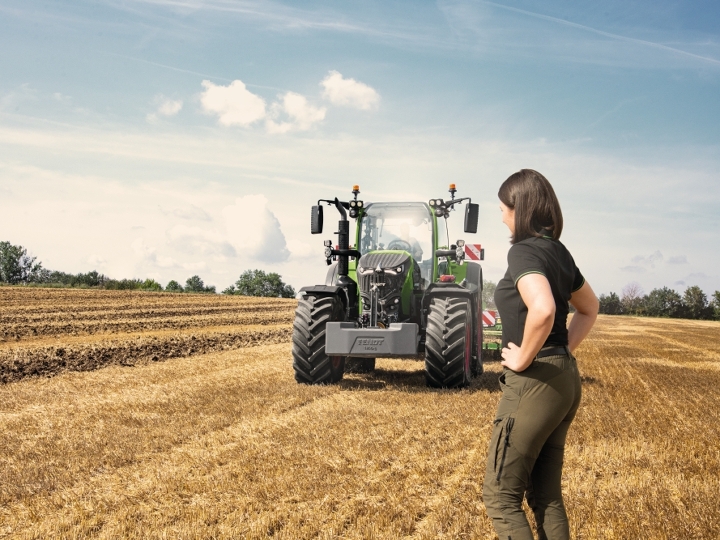 Une agricultrice se tient fièrement devant son tracteur Fendt 700 Vario Gen7 dans un champ de chaume.