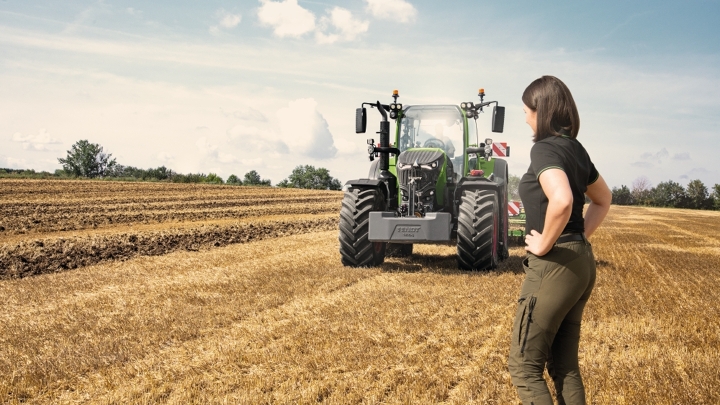 Une agricultrice se tient fièrement devant son tracteur Fendt 700 Vario Gen7 dans un champ de chaume.