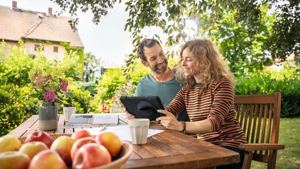 Un couple d’agriculteurs est assis à une table de jardin devant sa tablette et vérifie son éligibilité à Fendt Connect