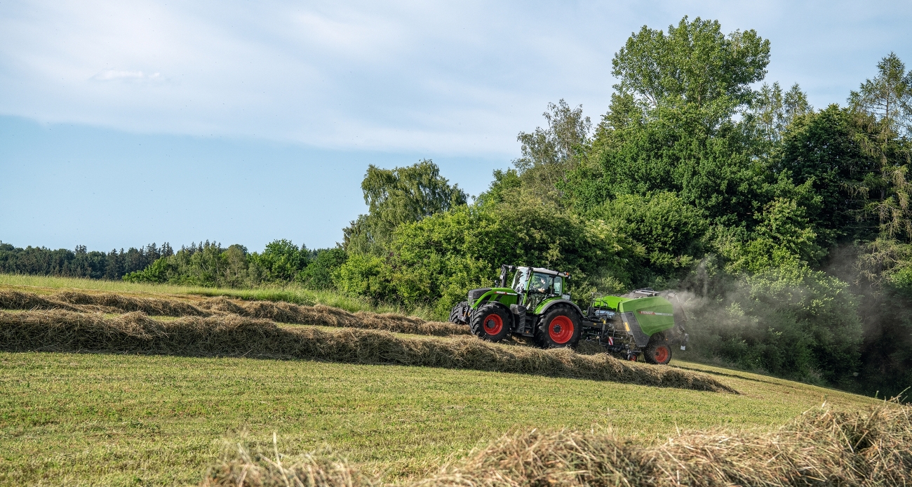 Fendt 700 Vario és Rotana 180 V Xtra a zöld takarmány betakarítása közben. A háttérben fák és bokrok láthatók.