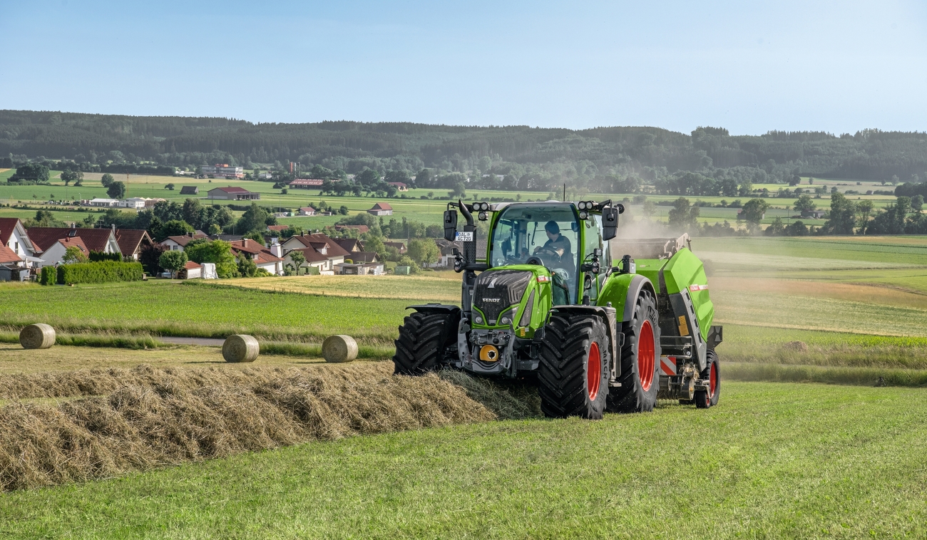 Fendt 700 Vario Rotana 180 V Xtra körbálázóval egy falu szélén, füves területen