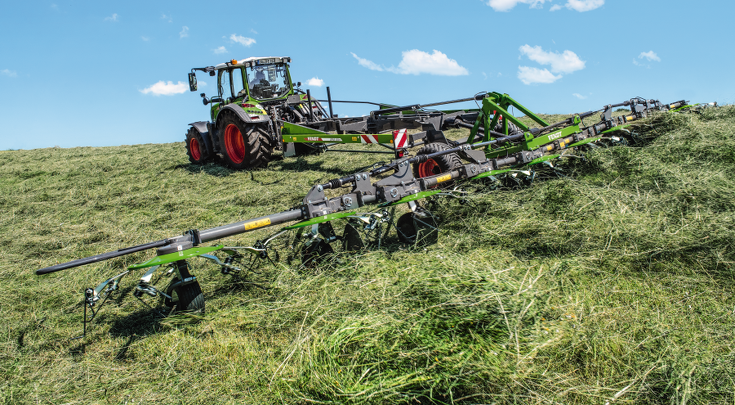 gy zöld Fendt traktor a zöld Fendt Lotus-szal használat közben egy mezőn, fű terítésekor, kék égbolttal a háttérben