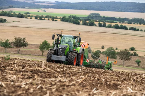 A Fendt 728 Vario with an implement on a field further fields and forests in the background