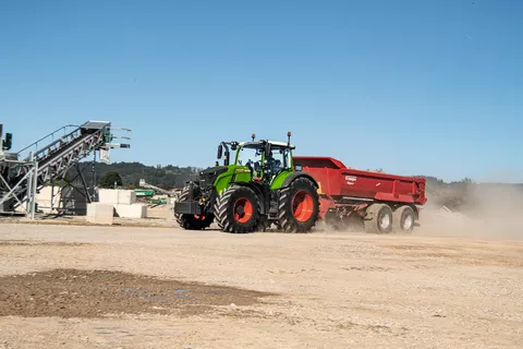 A Fendt 700 Vario Gen7 is driving on a construction site with a red Krampe tipper, raising clouds of dust.