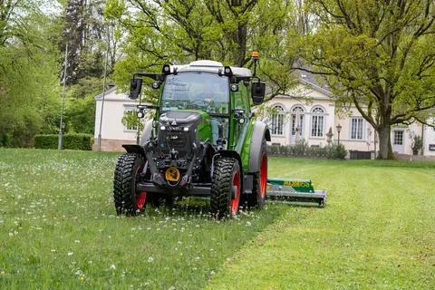 A Fendt e107 Vario mowing a meadow in a park in front of a historic building