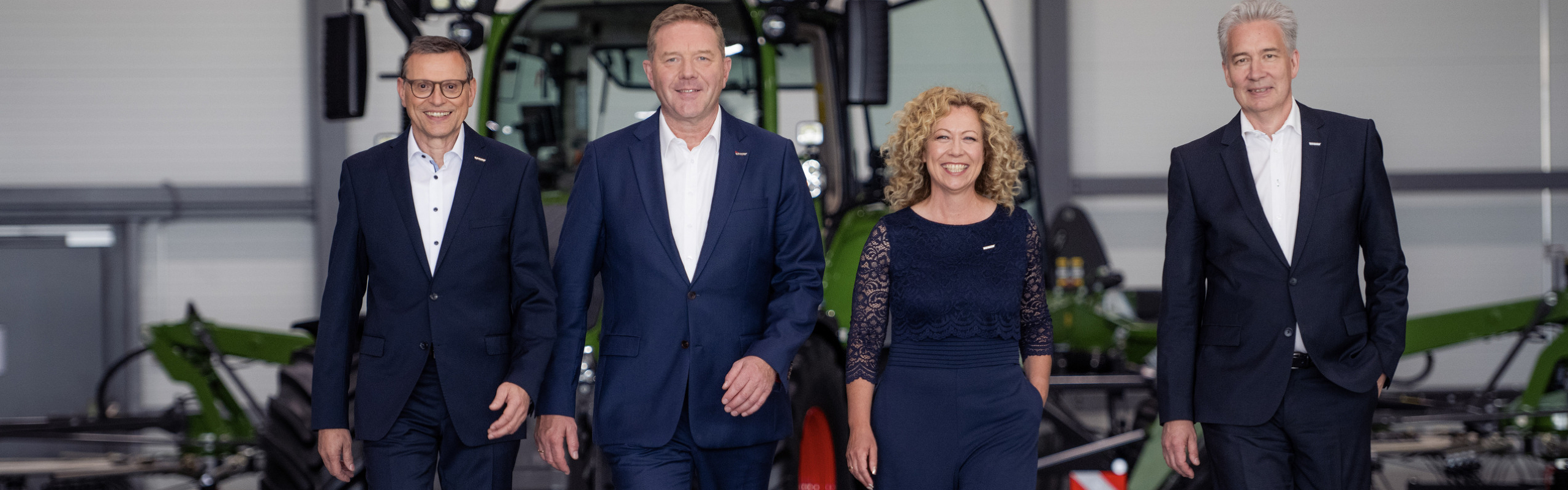 Walter Wagner, Christoph Gröblinghoff, Ingrid Bußjäger-Martin and Ekkehart Gläser standing next to each other in the Fendt Forum in front of a Fendt tractor and smiling.