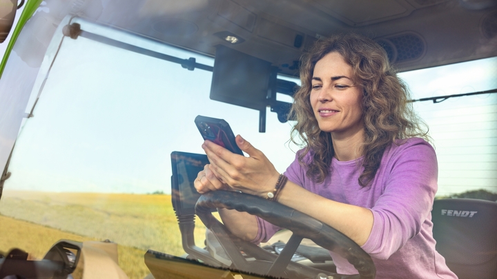 A farmer on her tractor checking for Fendt services on her mobile phone