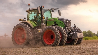 A farmer driving a Fendt 700 Vario Gen7 with dual wheels in the field and a lot of dust is stirred up.