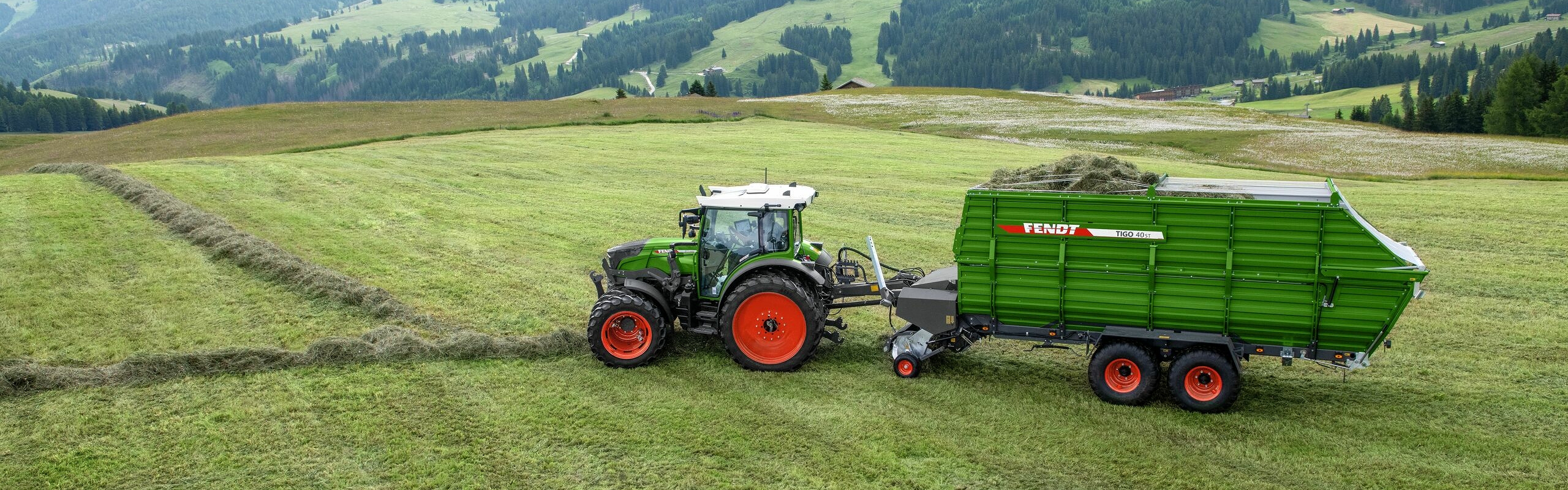 A green painted Fendt 200 Vario with attached Tigo forage wagon in alpine use