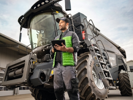 A Fendt service employee stands in front of an IDEAL combine harvester with a tablet in his hand.