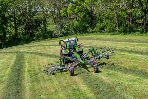 A Fendt tractor drives on a green field with a Fendt Former rake.