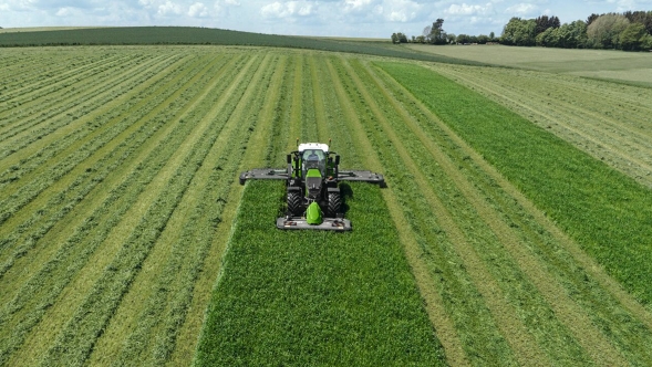 A farmer mows a green meadow with a Fendt Slicer mower combination.