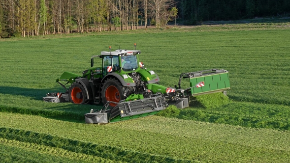 A farmer mows a green meadow with a Fendt Slicer mower combination.