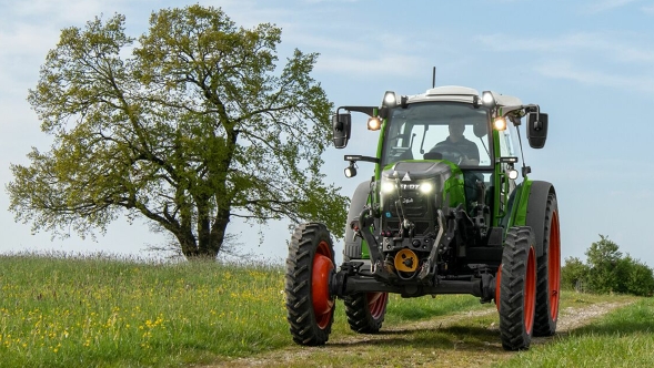 A green Fendt e100 Vario travelling along a meadow path in spring